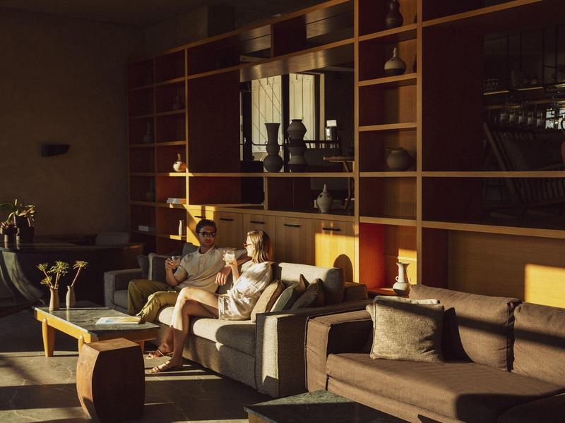 Przytulna przestrzeń wypoczynkowa z sofami, siedzącą kobietą, ciepłym światłem i drewnianymi półkami.