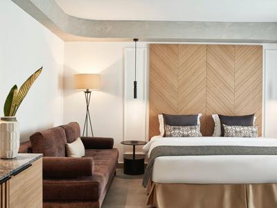 Modern hotelkamer met gezellig bed, bank, vloerlamp en minimalistische inrichting.