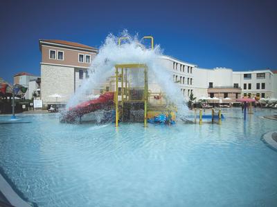 Groot zwembad met waterpark en waterspelletjes voor gebouwen onder een heldere lucht.