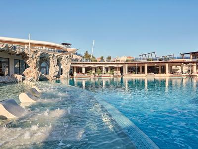 Modernes Hotel mit großem Pool und Wasserfontänen bei klarem Himmel.