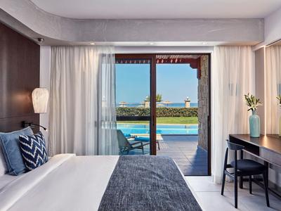 Moderní hotelový pokoj s postelí, pracovním stolem a výhledem na bazén a zahradu přes velké posuvné dveře.