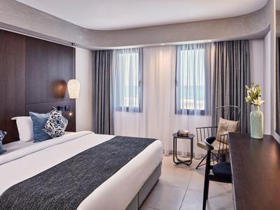 Moderne hotelkamer met groot bed, lichte muren en ramen met gordijnen.