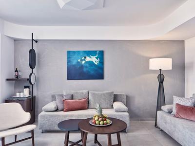 Modern woonkamer met grijze bank, tafel, stoel en een schilderij aan de muur.