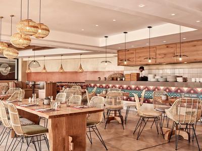 Licht en modern restaurant met houten en metalen stoelen en hanglampen.