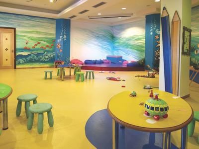 Kleurrijke speelkamer voor kinderen met tafels, krukjes en muurmuurschilderingen onder verlichting.