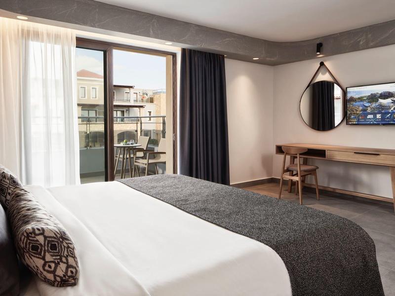 Moderne hotelkamer met groot bed, bureau en balkon met uitzicht op de stad.