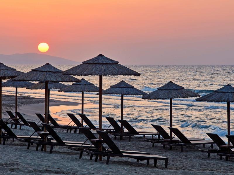 Zonsondergang boven de zee met zandstrand en lege ligstoelen onder parasols