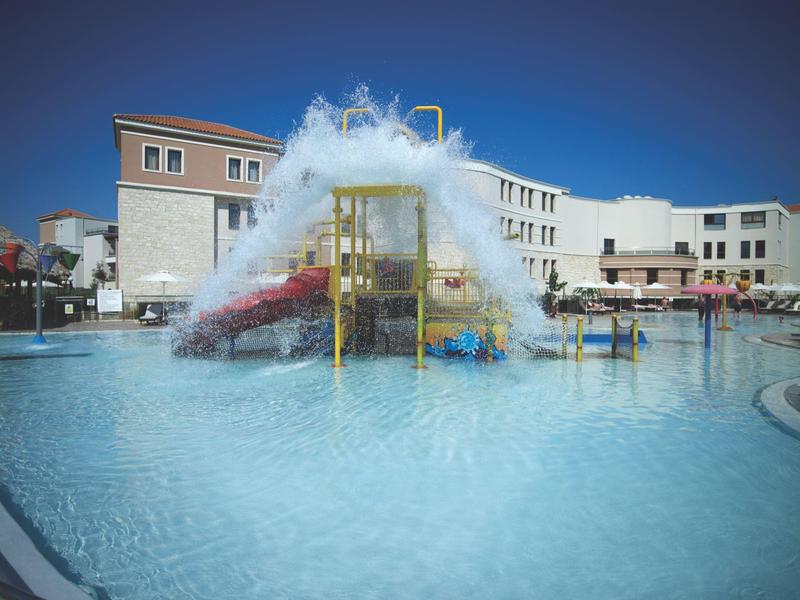 Groot zwembad met waterpark en waterspelletjes voor gebouwen onder een heldere lucht.