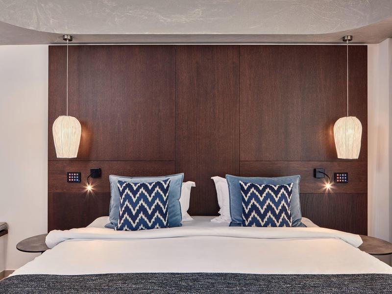 Moderne hotelkamer met groot bed, blauwe sierkussens en houten wand met twee hanglampen.