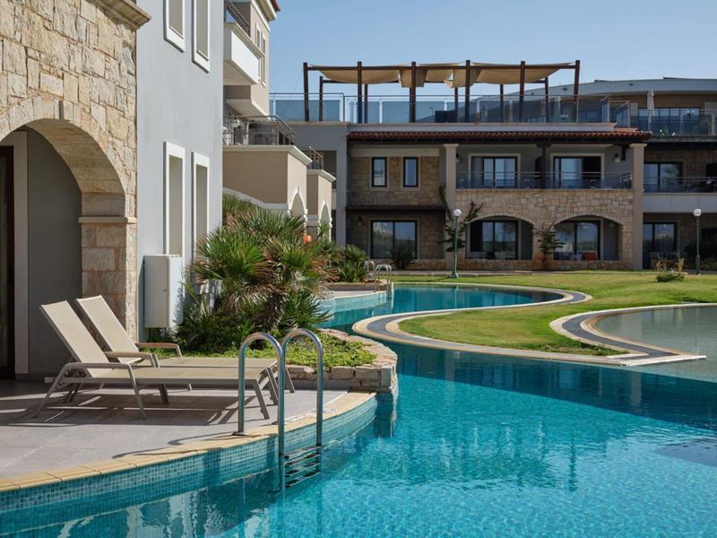 Zwembad met ligstoelen en moderne gebouwen op de achtergrond overdag.