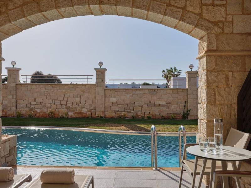 Zwembadgebied met boogdeur, tafel met glazen en geserveerd water, uitzicht op muur en lucht.