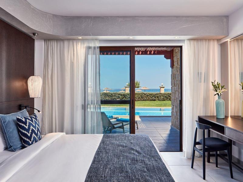 Slaapkamer met groot bed en uitzicht op een zwembad en zee door een glazen schuifdeur.