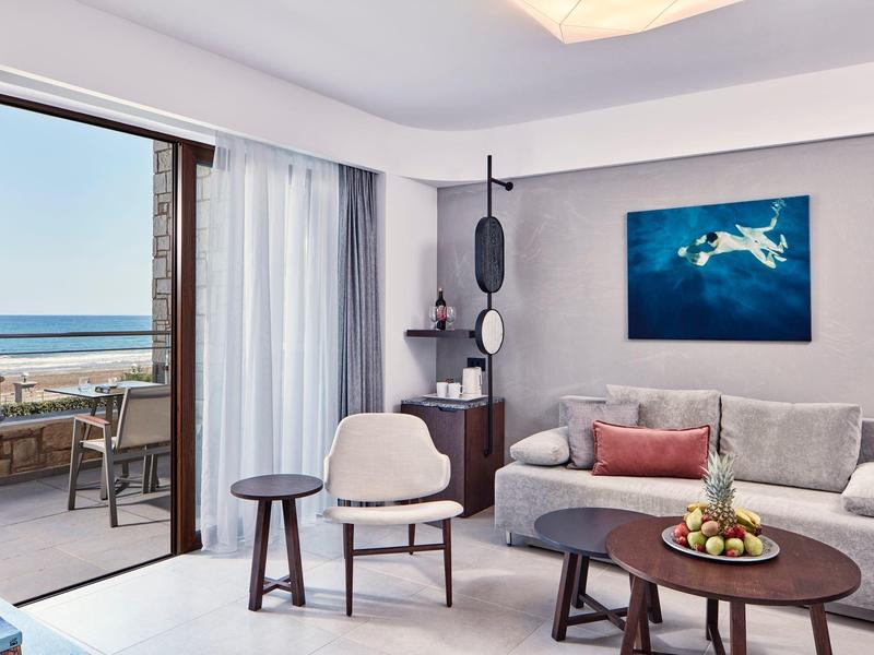 Moderne hotelkamer met bank, stoelen, balkon en uitzicht op zee.