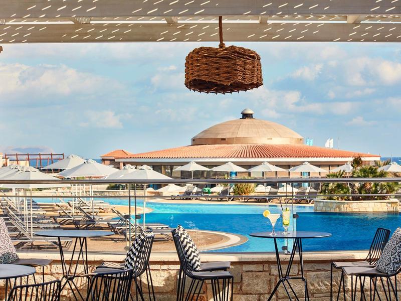 Uitzicht vanaf een overdekt terras met tafels en stoelen op een zwembad en een resort met een rond gebouw.