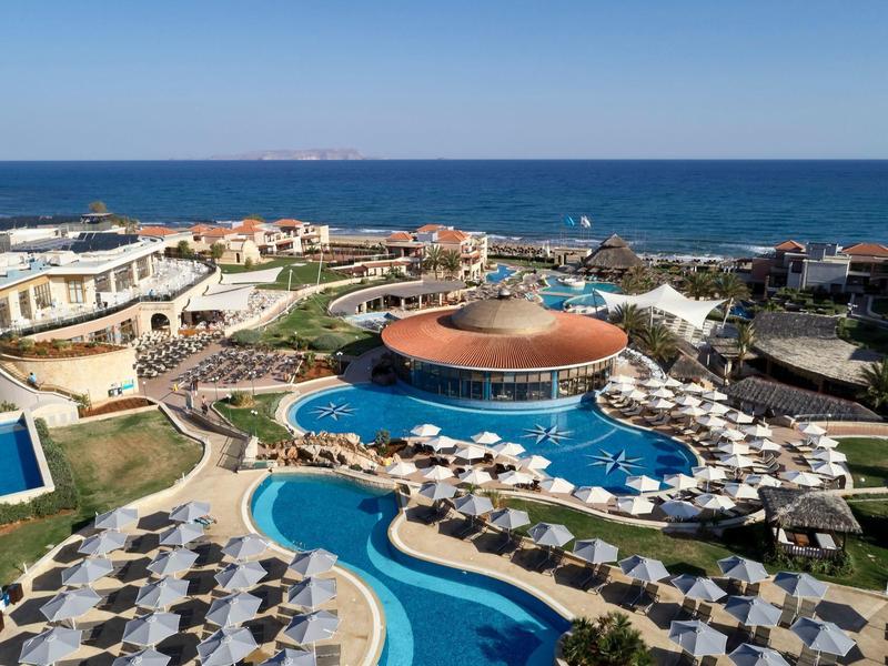 Uitzicht op een resort met meerdere zwembaden, parasols en de zee op de achtergrond.