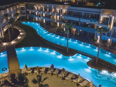 Verlicht hotelzwembad met ligstoelen en modern gebouw in de nacht
