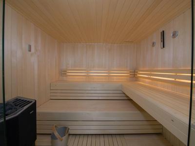 Sauna lumineuse en bois clair avec bancs en plusieurs niveaux et poêle à gauche.