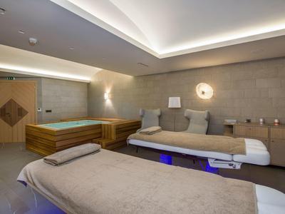 Salle de bien-être moderne avec tables de massage et bassins en bois sous lumière tamisée.