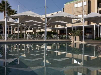 Een zwembad met meerdere witte parasols en een modern hotelgebouw op de achtergrond.