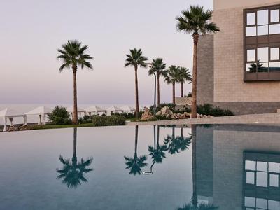 Ein ruhiger Pool spiegelt Palmen und ein Gebäude bei sanftem Abendlicht.