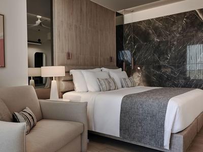 Camera d’hotel moderna con letto grande, poltrona e arredamento elegante dai toni neutri.