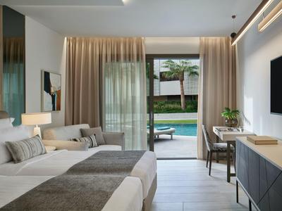 Camera d'hotel moderna con due letti, angolo salotto accogliente e vista su una piscina.