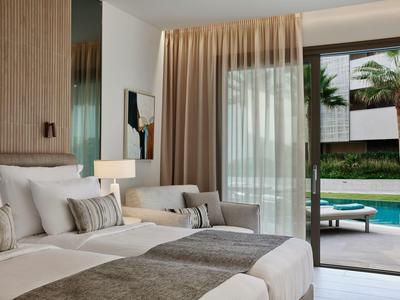 Camera d'hotel moderna con due letti, tende e vista su un'area piscina con palme.