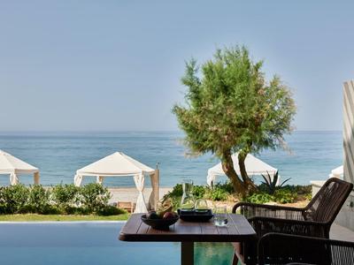Uitzicht op zee met witte paviljoens en een boom naast een tafel met stoelen op een terras.
