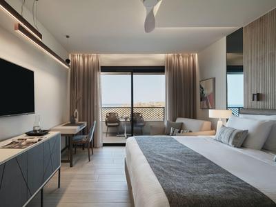 Chambre d'hôtel moderne avec balcon, grand lit et télévision murale.