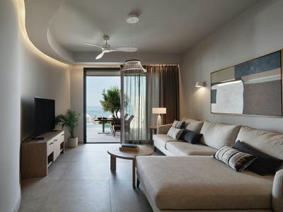 Salon moderne avec canapé, télévision et accès à un balcon avec vue sur la mer.