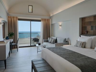 Chambre d'hôtel moderne avec grand lit et vue sur la mer depuis le balcon.