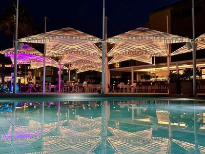 Bar de piscine éclairée avec parasols et reflet dans la piscine la nuit