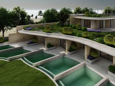 Modern hotel complex with private pools, terrace, and green surroundings by the water.