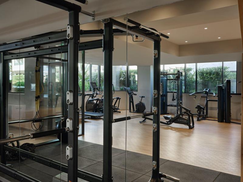 Salle de sport moderne avec divers équipements d'entraînement et grandes fenêtres en arrière-plan.