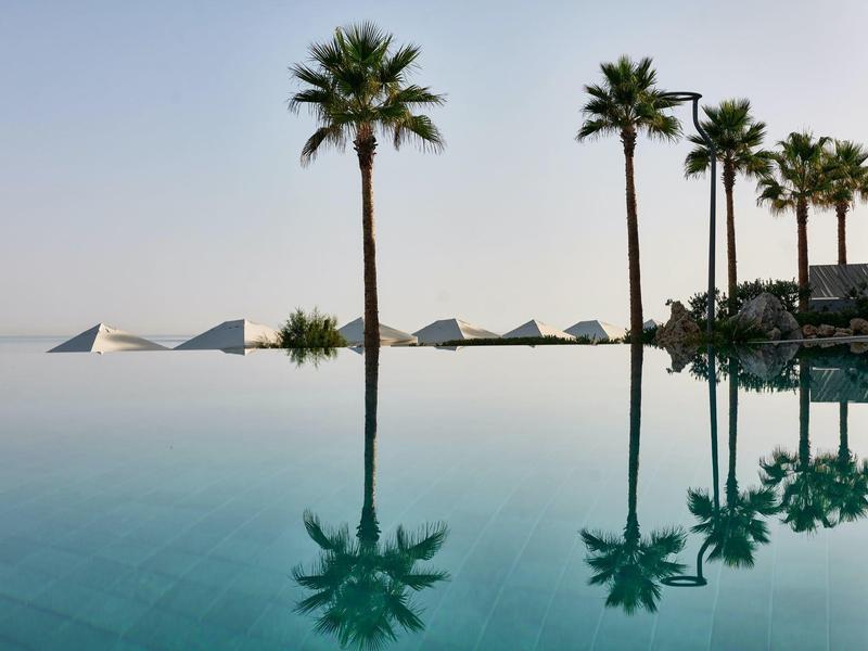 Piscine à débordement avec palmiers et pyramides à l'horizon sous un ciel clair et calme.