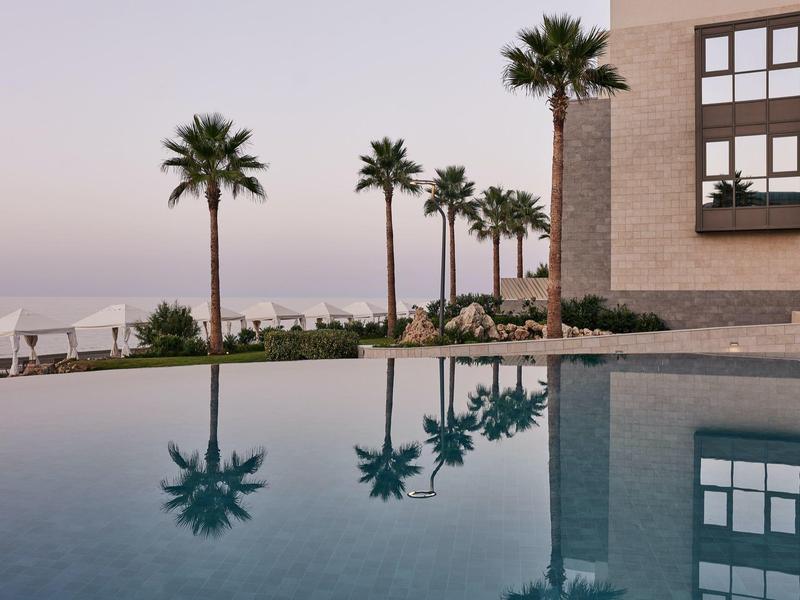 Vue sur une piscine avec des palmiers et un bâtiment en arrière-plan au coucher du soleil.