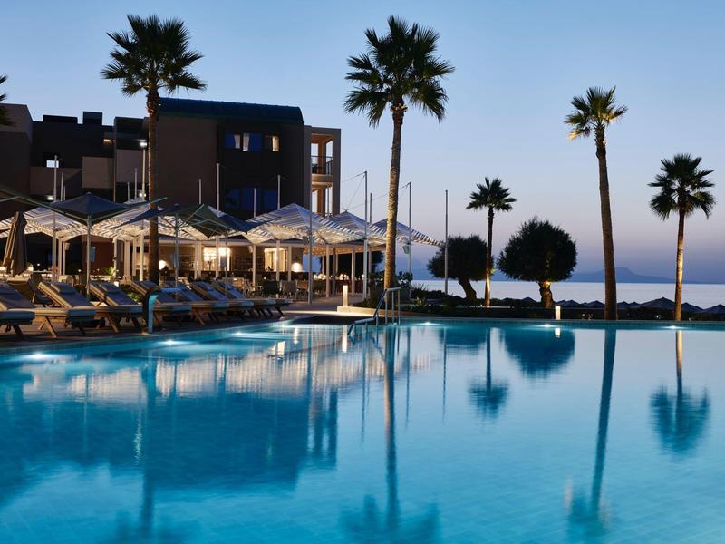 Piscine d'hôtel luxueuse au crépuscule avec palmiers et chaises longues près de la mer.