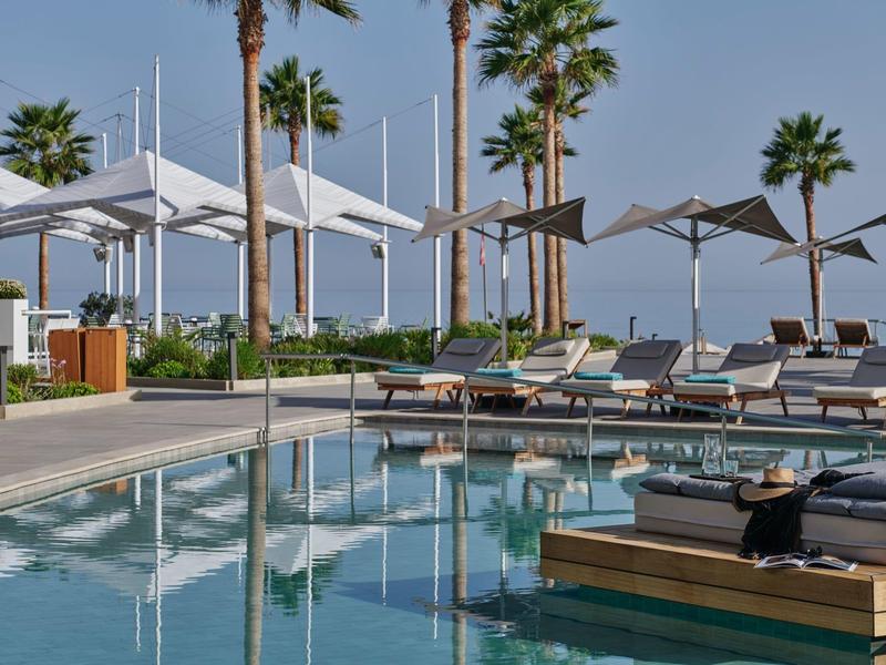 Piscine d'hôtel moderne avec chaises longues, parasols et palmiers par une journée claire.