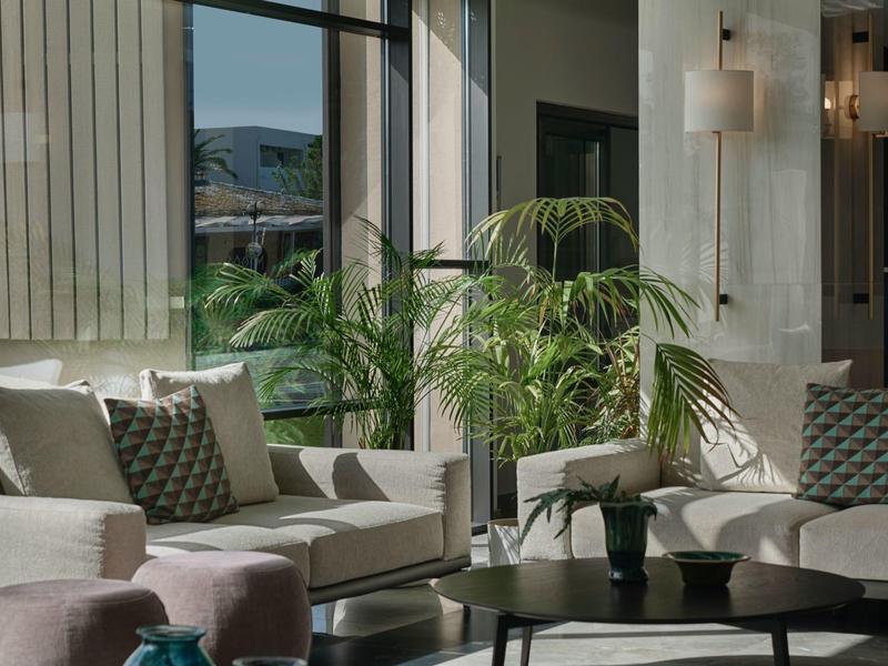 Chambre d'hôtel lumineuse avec canapé, plantes et table basse moderne.