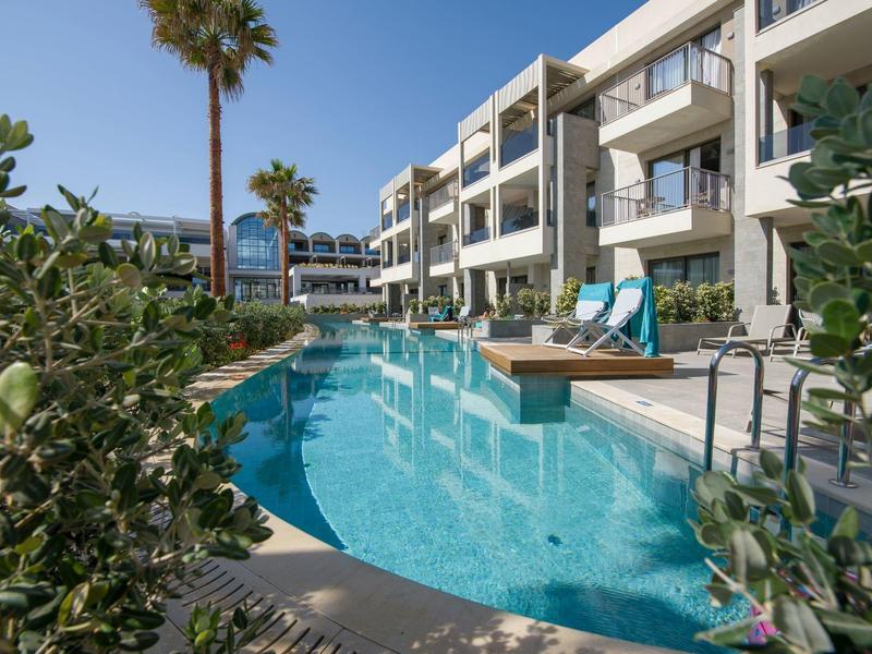 Complex hôtelier moderne avec piscine extérieure et chaises longues sous un ciel clair.
