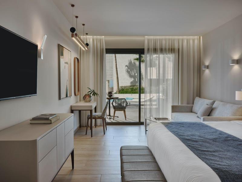 Chambre d'hôtel moderne avec lit double, bureau, TV et balcon avec vue sur la verdure.