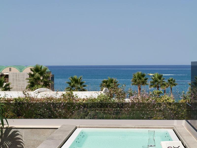 Piscine moderne avec vue sur la mer et palmiers en arrière-plan sous un ciel clair.