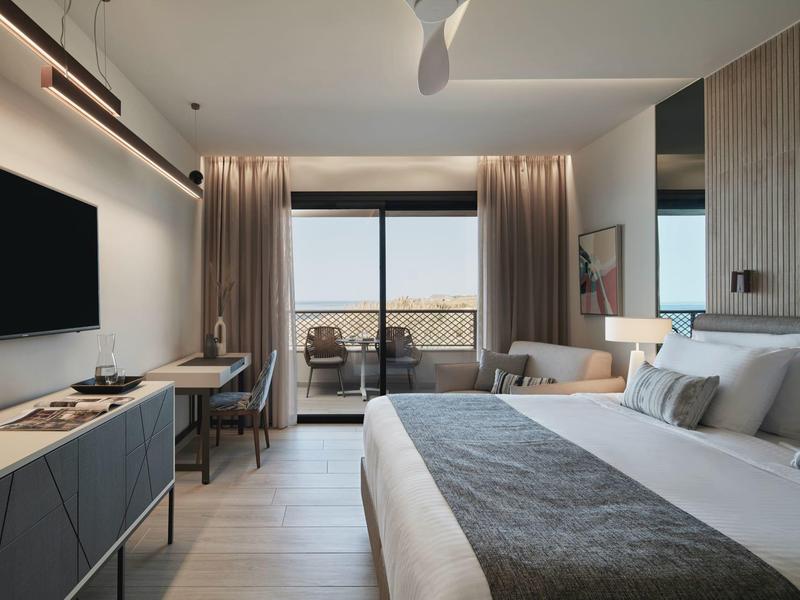 Chambre d'hôtel moderne avec balcon, grand lit et télévision murale.