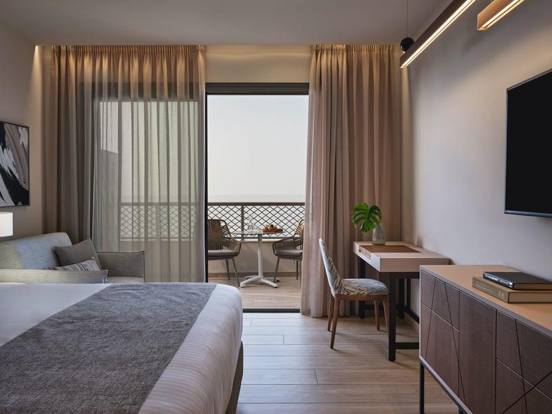 Chambre d'hôtel moderne avec grand lit, bureau et balcon avec sièges.