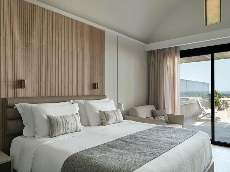 Chambre d'hôtel moderne avec grand lit, panneau en bois et terrasse vue mer.