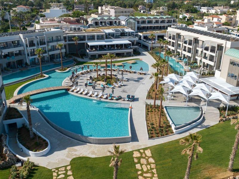 Grand complexe hôtelier avec plusieurs piscines, chaises longues et bâtiments autour ensoleillés.