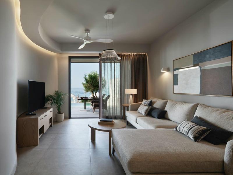 Salon moderne avec canapé, télévision et accès à un balcon avec vue sur la mer.