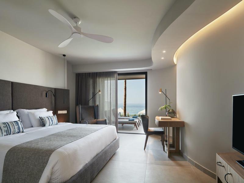 Chambre d'hôtel moderne avec grand lit, bureau et balcon offrant une vue sur la mer.