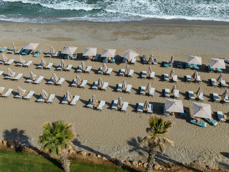 Rangées de chaises longues et parasols sur une plage de sable face à la mer.