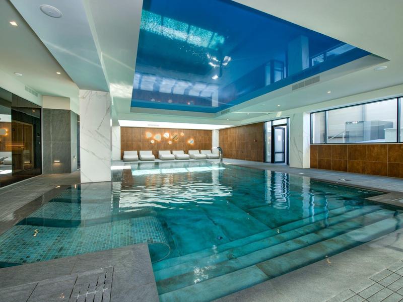 Piscine intérieure moderne avec plafond bleu réfléchissant et grandes fenêtres.